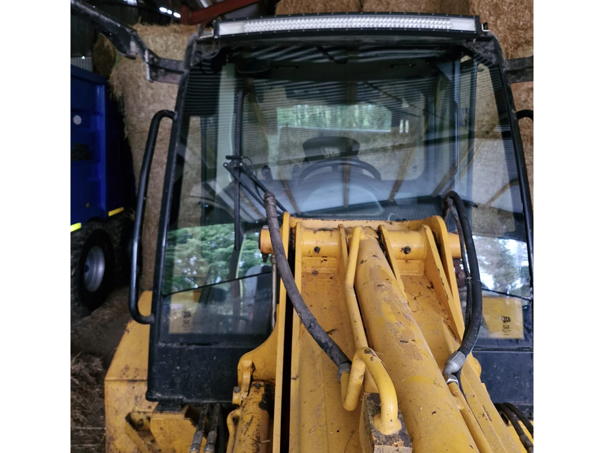 JCB backhoe loader with a newly fitted front cab windscreen in a hay barn
