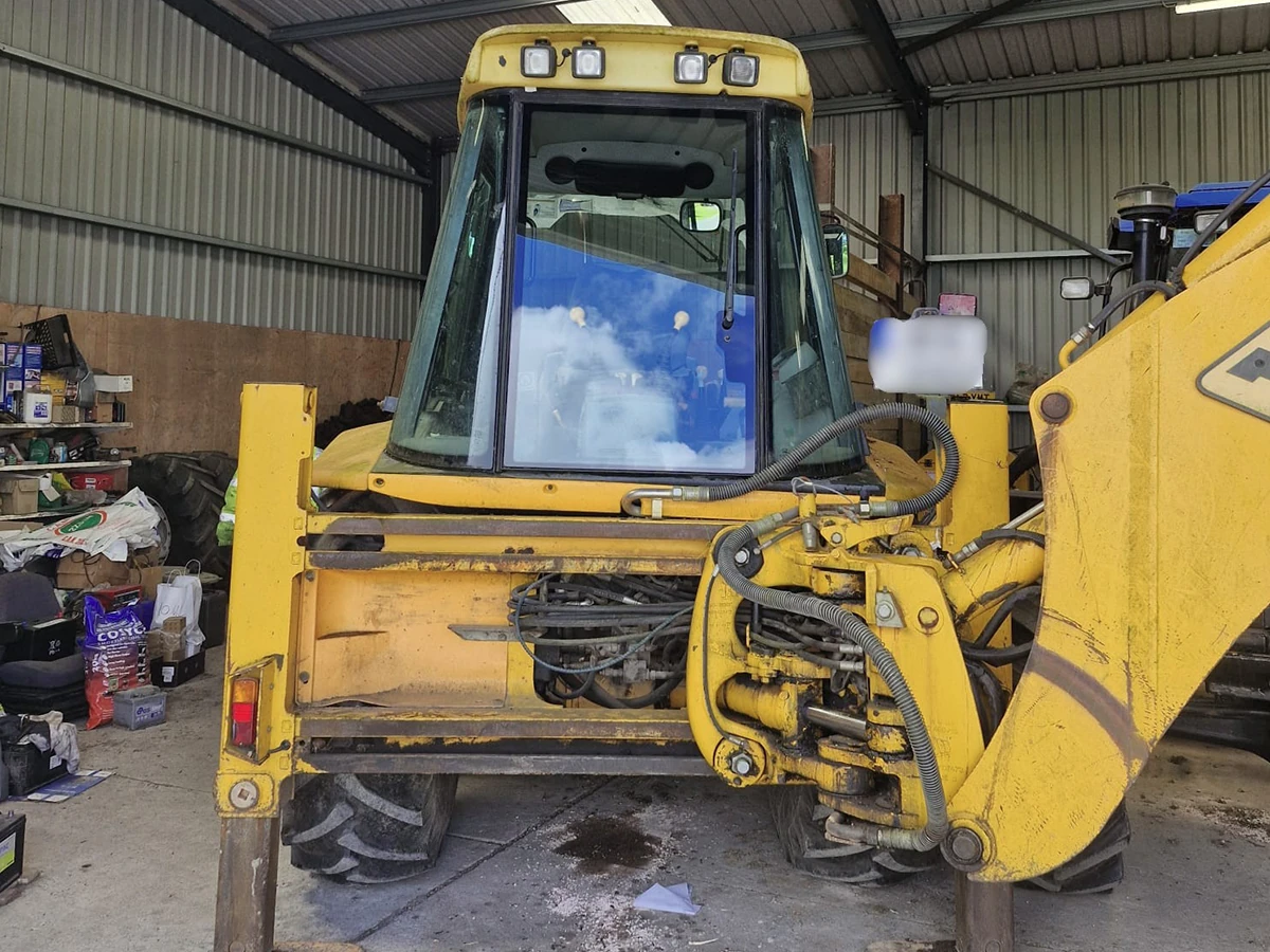 Yellow JCB backhoe loader with a replacement front windscreen in a farm shed