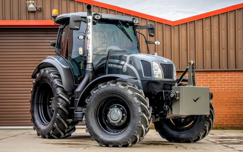 Black New Holland tractor with full replacement cab glass parked outside the workshop